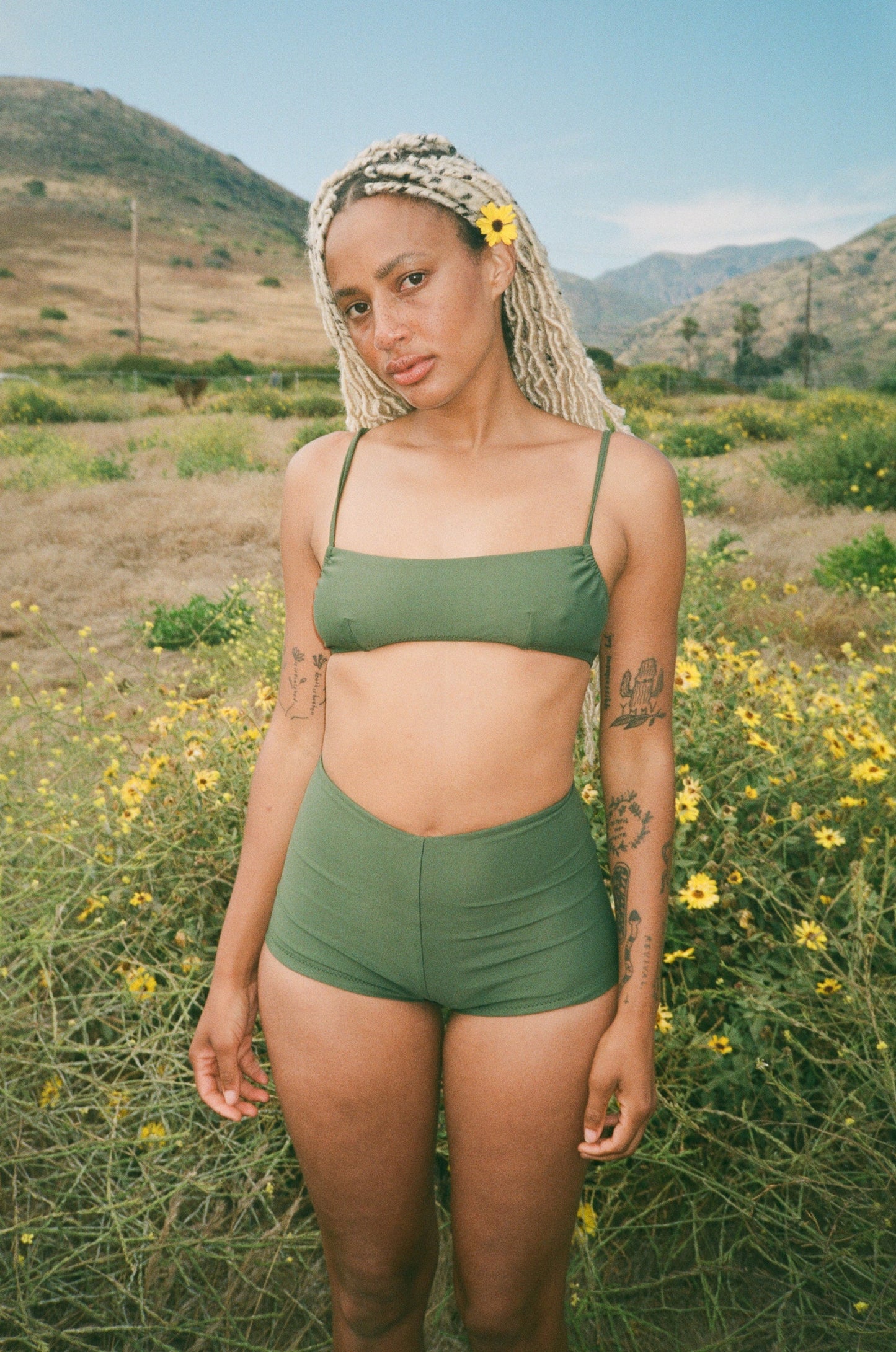 Woman in green swimsuit  standing in a field with flowers and mountains in the background